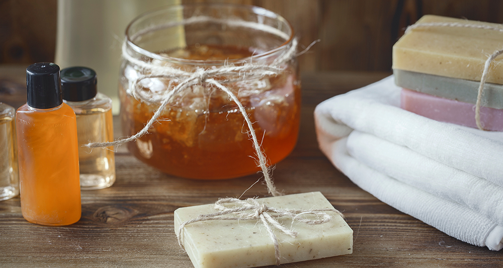 Bath towels, soaps and shampoos on a table with a jar of honey.