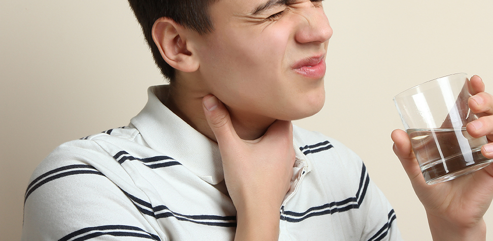 Man drinking glass of water holding hand to his throat with look of pain on face.