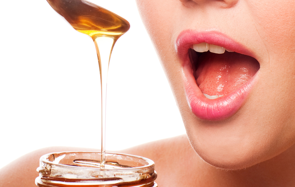 Person with mouth open preparing to eat honey from a spoon.