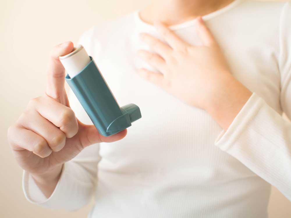 person holding asthma inhaler with hand to chest 