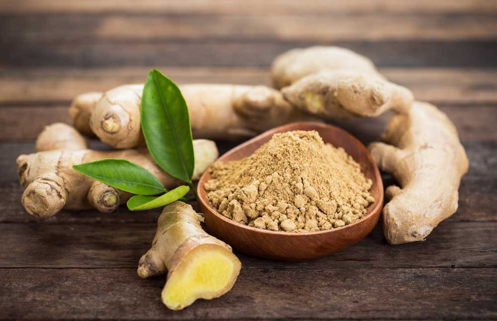 Ginger root on wooden surface with bowl of powdered ginger