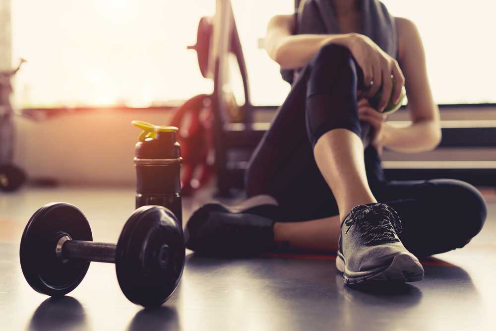 Person sitting on gym floor with water bottle and dumbell